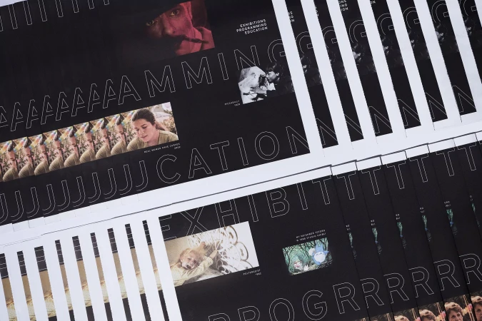 Stacks of black and white posters promoting exhibitions, programming, and education with various images and large typography.