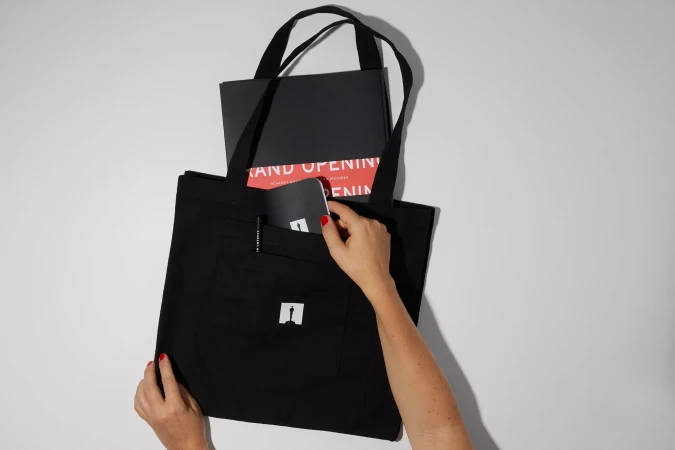 Cropped shot of a woman's arm reaching into a black tote bag containing a notebook and a brochure on a clean, white background.