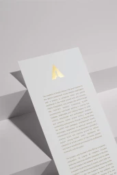 White paper card with gold foil logo and printed text placed on geometric white surfaces with soft shadows.