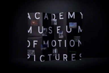 Folded black paper brochure featuring bold white typography reading Academy Museum of Motion Pictures and embedded imagery.