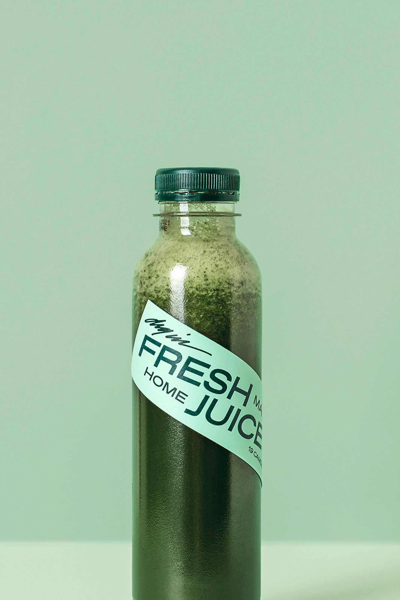 A bottle of dark green juice with a light green label that reads 'Fresh Home Juice' stands against a soft green background.