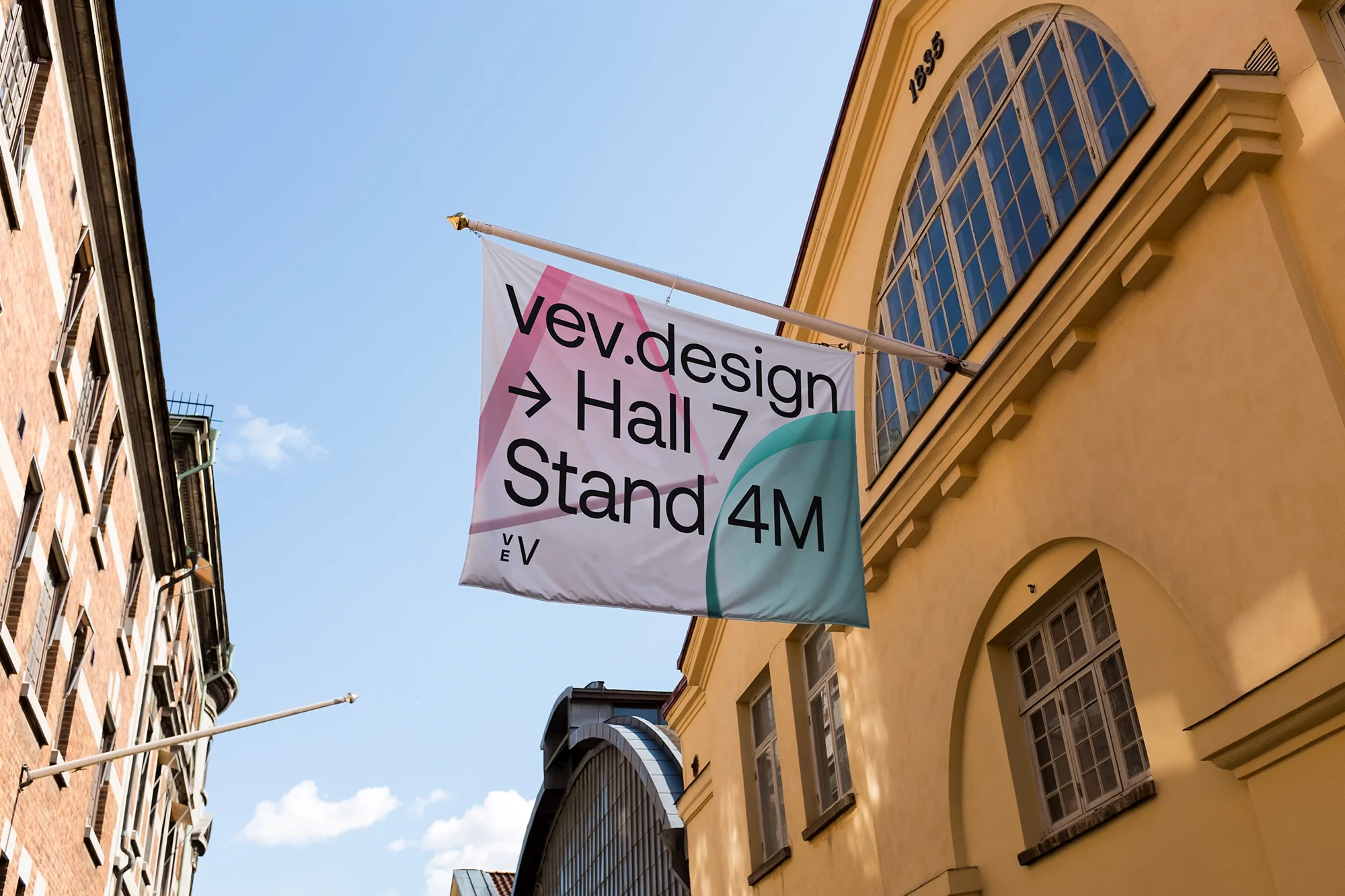 Architectural photograph features a large banner ad for vev.design Hall 7 Stand 4M affixed to the exterior of a tan-colored building.