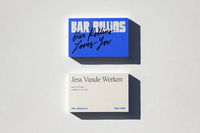Two business cards, one blue with 'Bar Rollins Loves You' and one white with 'Jess Vande Werken,' set against a clean white surface.
