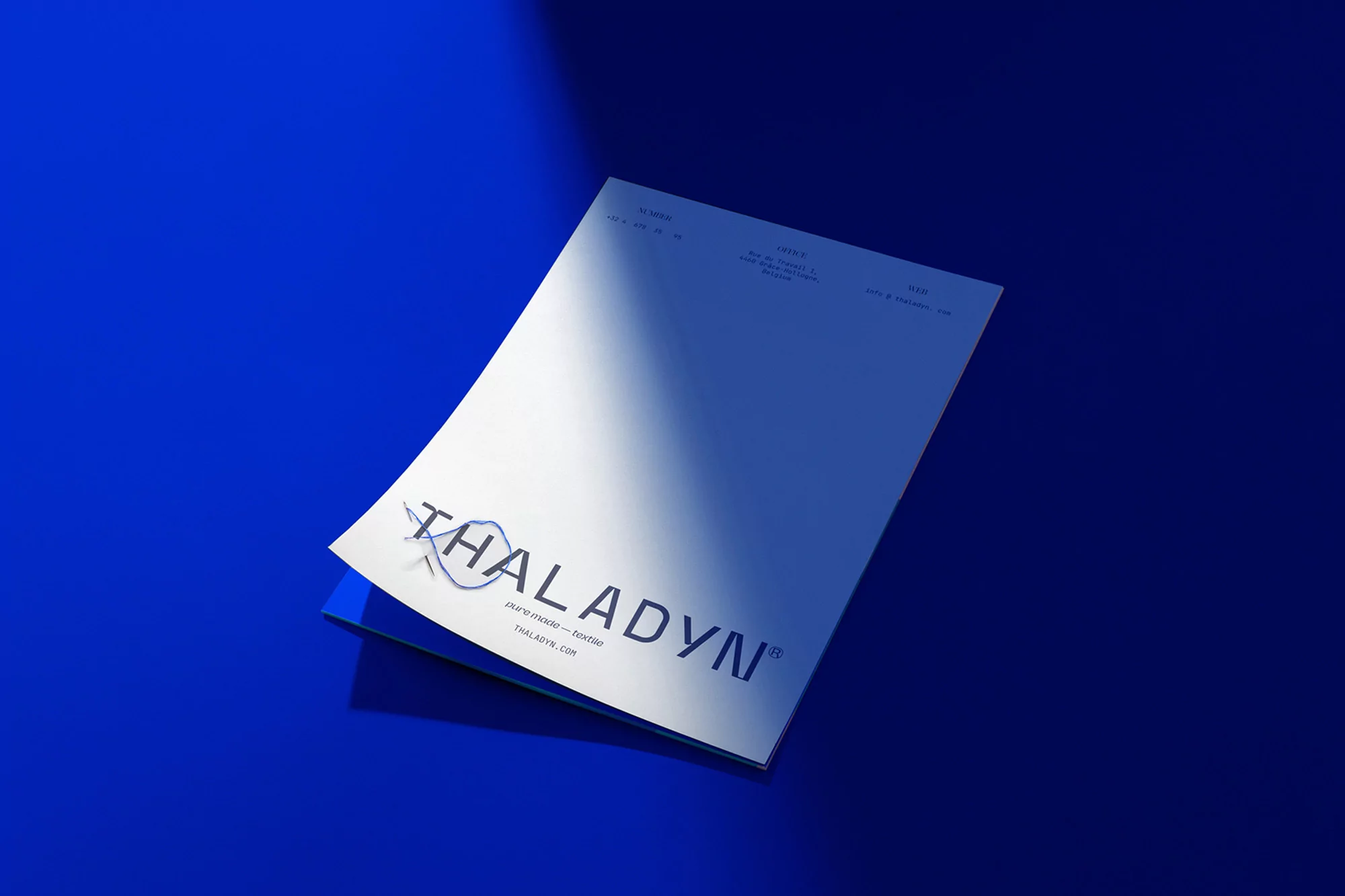 White letterhead paper with Thaladyn logo on a blue surface with natural light creates a clean, minimalist stationery aesthetic.