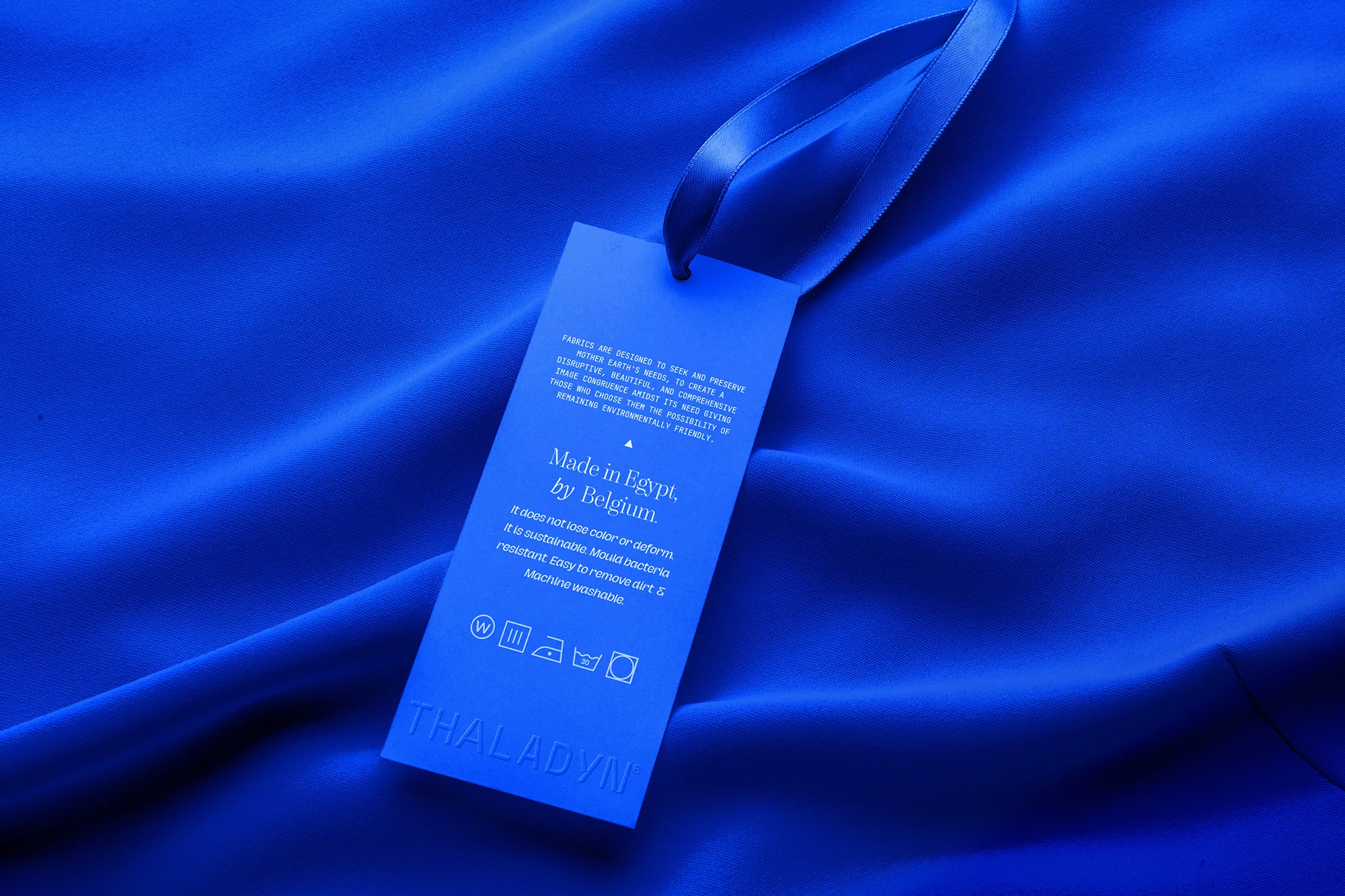 Close-up studio shot of a blue garment with a tag, highlighting the material and design in a monochromatic palette.