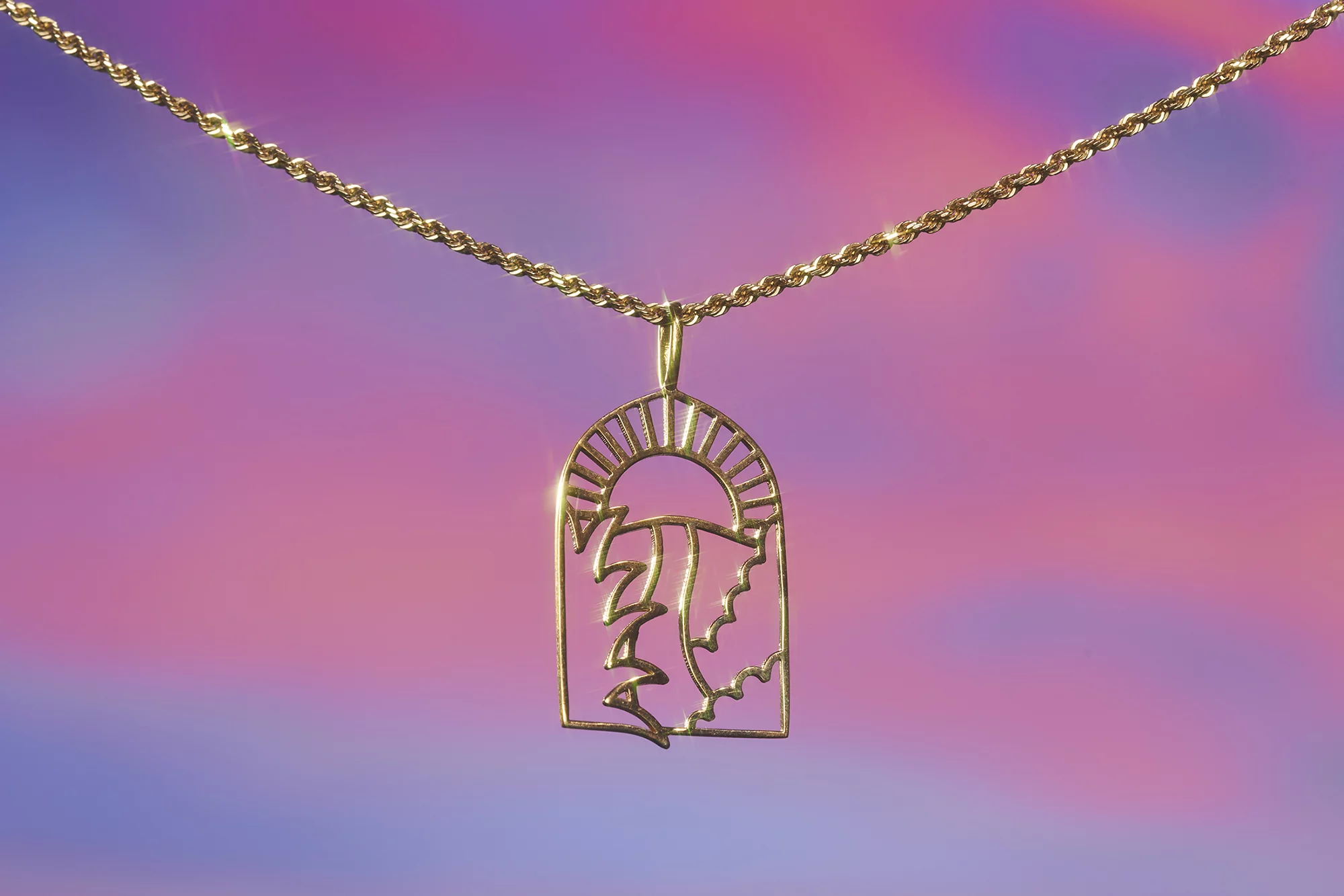 Gold necklace with an abstract sun pendant, featuring a unique design against a gradient background of pink, purple, and blue tones.