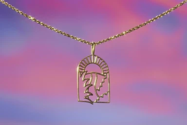 Gold chain necklace with an arched pendant featuring a sun and landscape design against a dreamy pink and blue gradient sky background.
