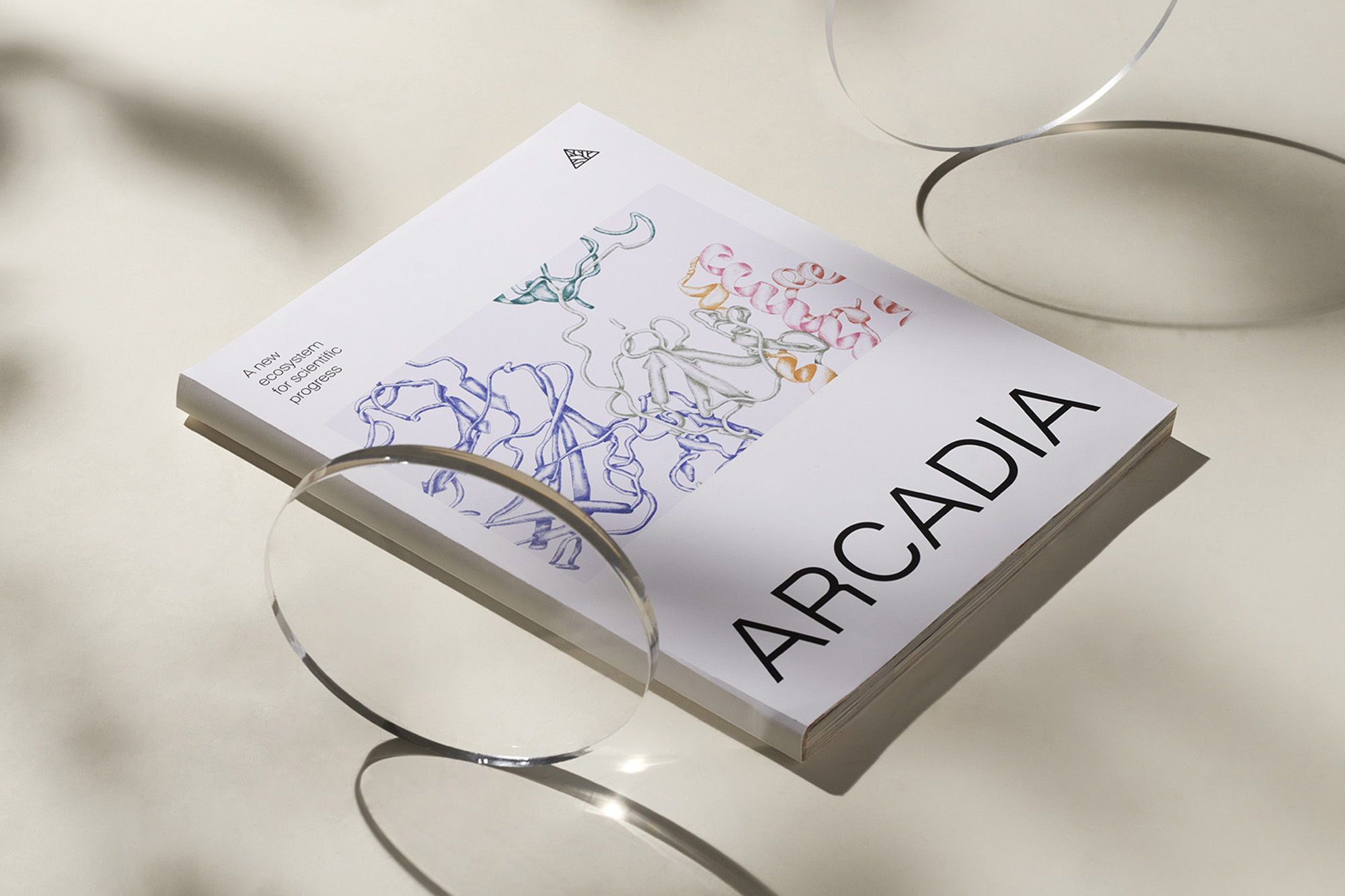 Arcadia magazine cover featuring colorful graphic design, book lying on a neutral surface with lens reflections creating visual interest.