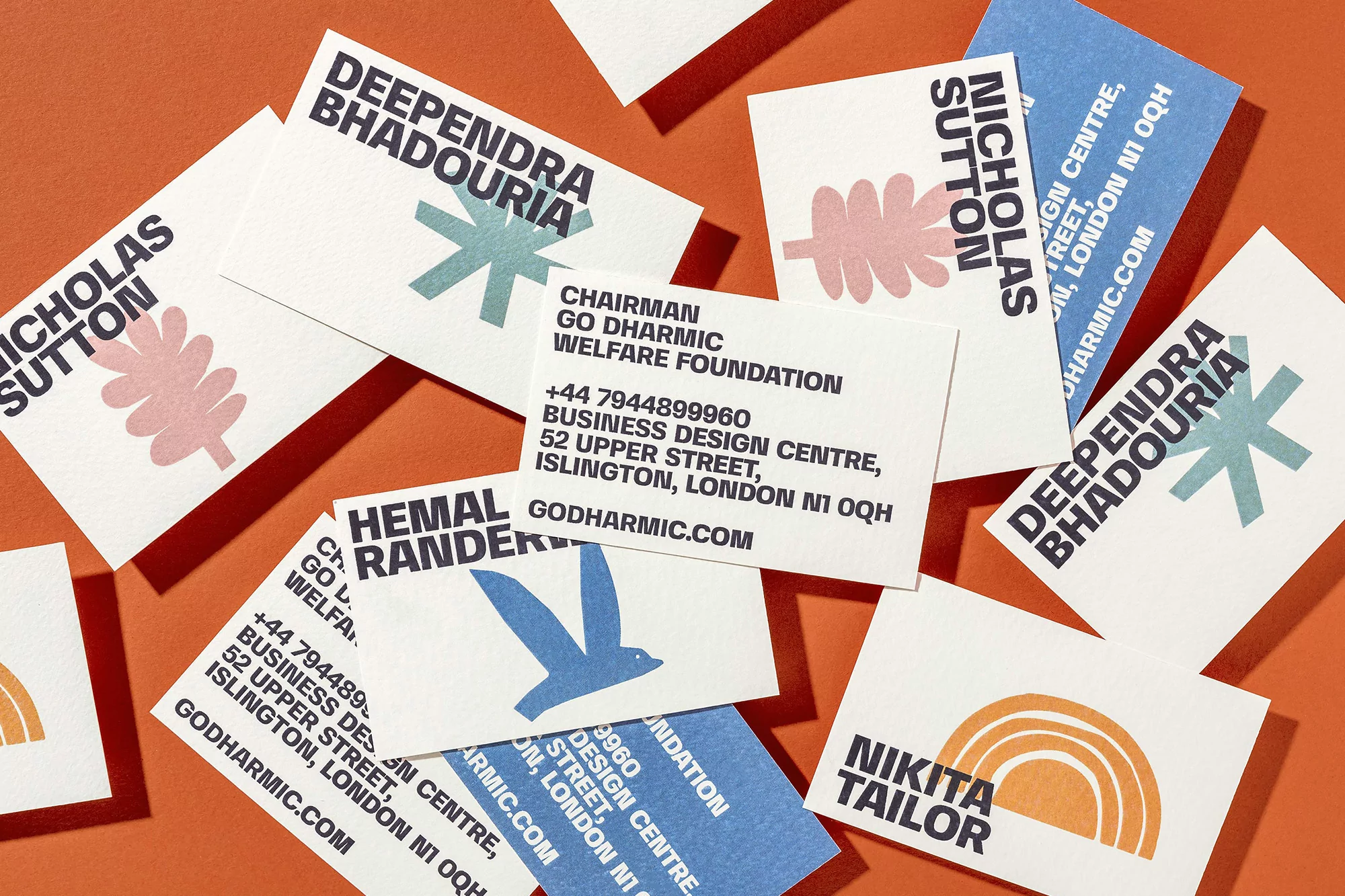Elevated view of business cards scattered on an orange surface. The cards have the names and company information printed, plus simple graphic design.