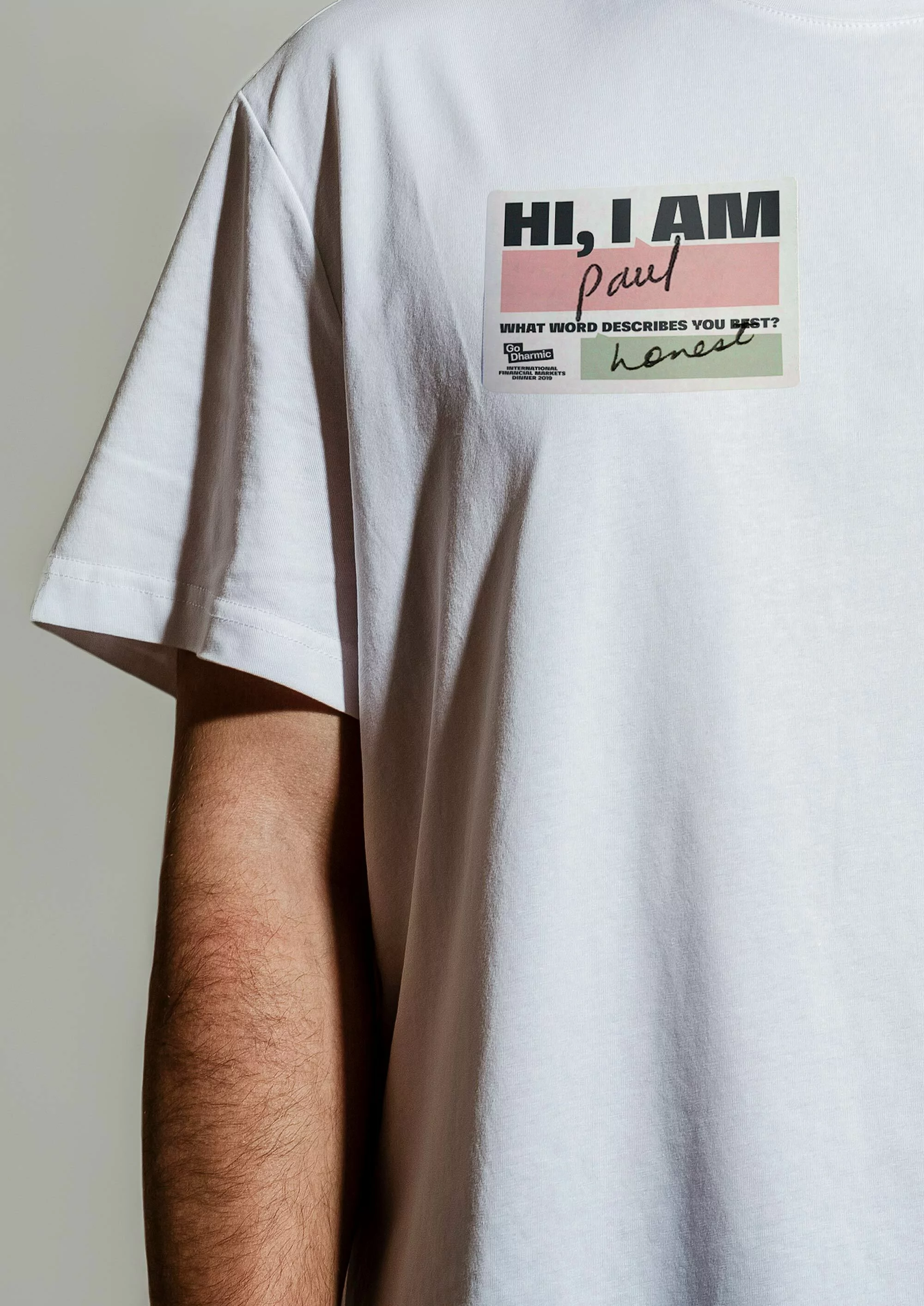 Man wearing a white t-shirt with a graphic text block that says 'Hi, I am Paul' and 'What word describes you best? Honest'.