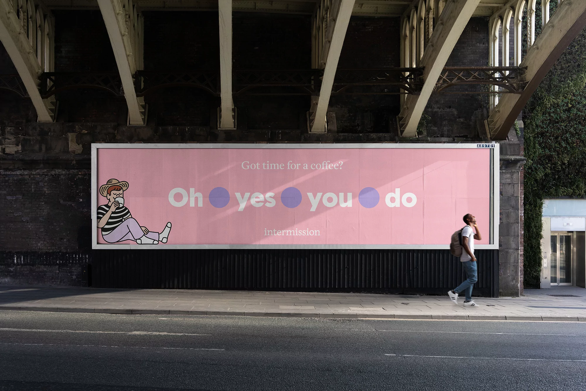 Illustrated figure on a pink billboard, advertising coffee, with a person walking past; located under a bridge, urban environment.