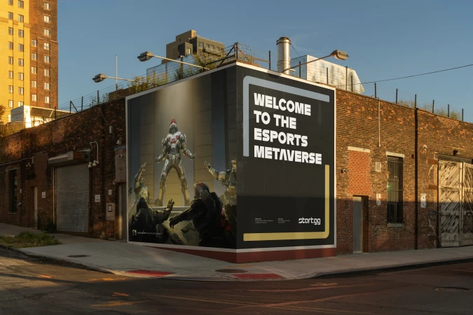 Outdoor billboard featuring a video game scene and the words 'Welcome to the Esports Metaverse' on a brick building in an urban setting.