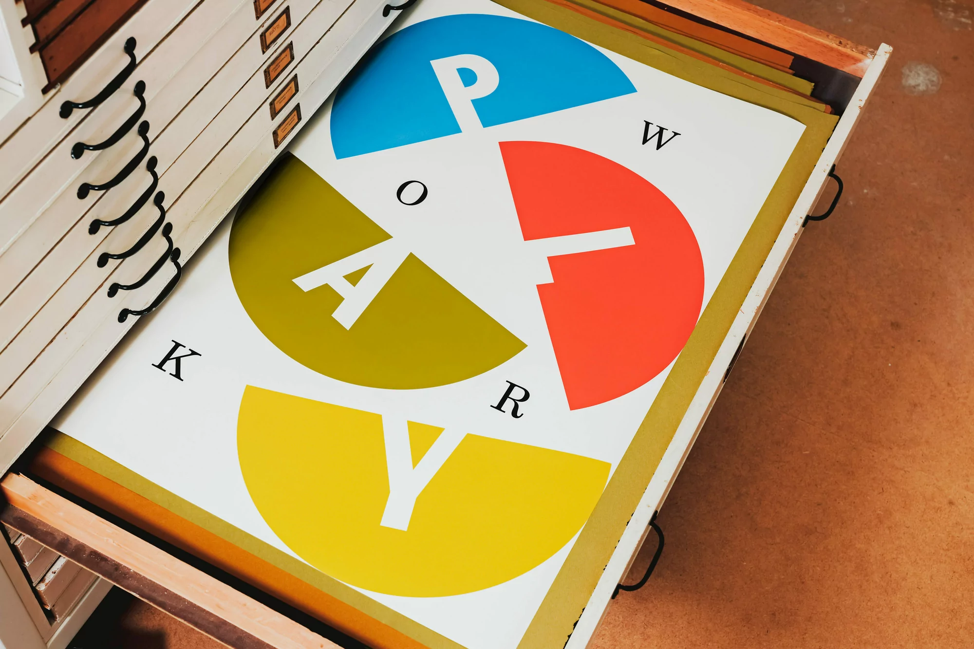 Open drawer shows colorful graphic art print with overlapping circles and the word 'WORKPLAY' in a clean, geometric sans-serif font.