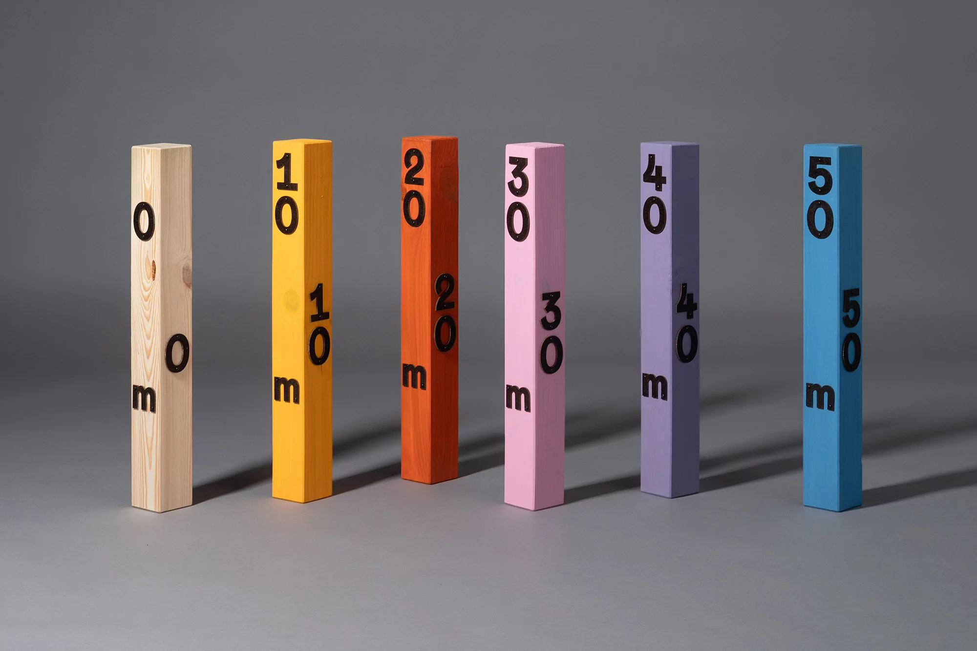 Colorful wooden blocks with increasing numbers '0m', '10m', '20m', '30m', '40m', '50m' stand in a row on gray surface, studio lit.