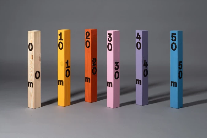 Colorful wooden blocks with increasing numbers '0m', '10m', '20m', '30m', '40m', '50m' stand in a row on gray surface, studio lit.
