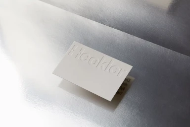 White embossed business card resting on a reflective metallic silver paper background with soft shadows