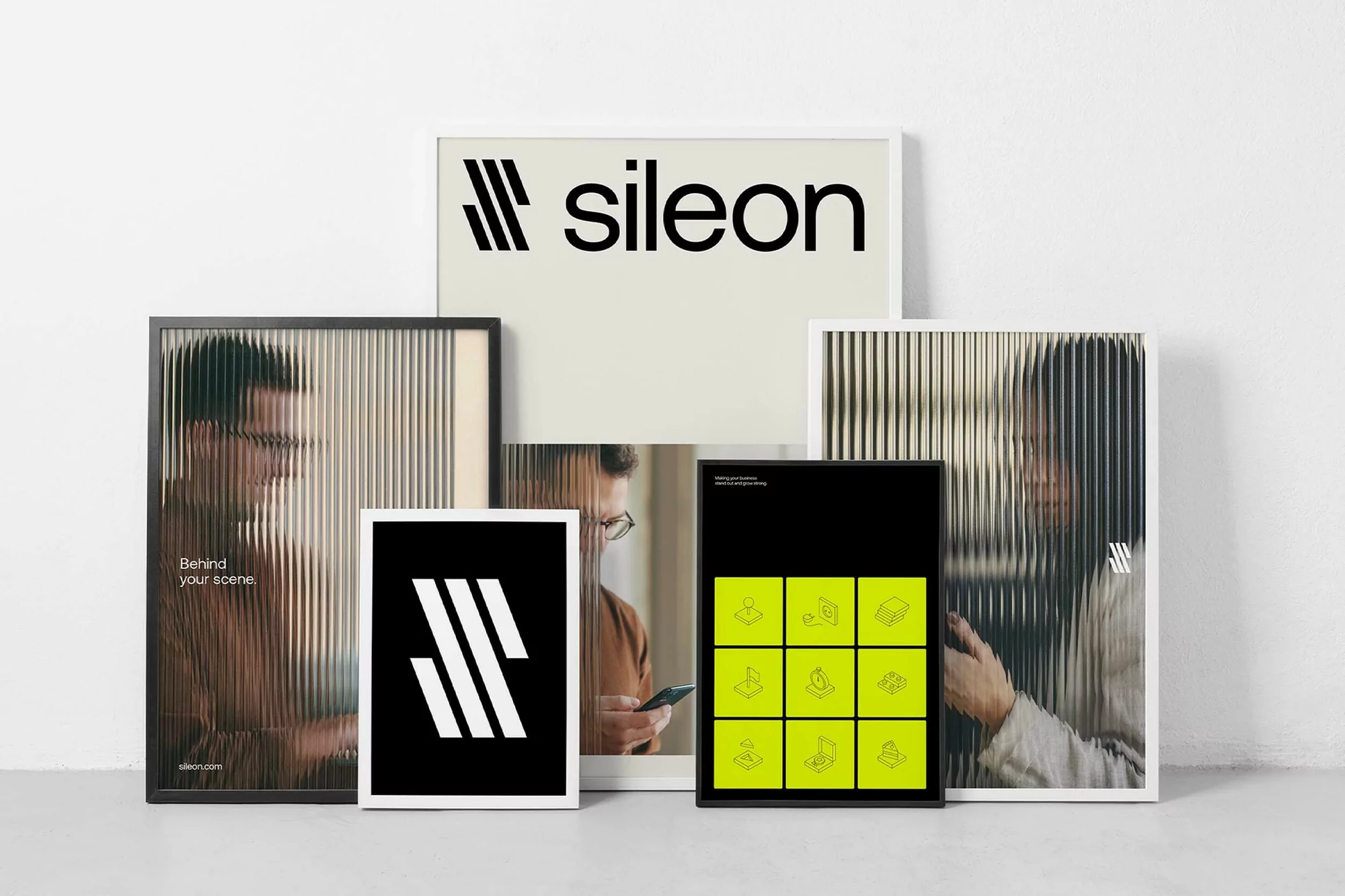 Several framed posters are leaning against a white wall, with black lettering and graphic elements in a bright, naturally lit interior.