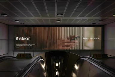 Large horizontal billboard for Sileon mounted above public transit escalators featuring vertical abstract imagery and typography