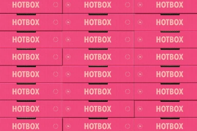 Stack of bright pink Hotbox pizza boxes with white typographic branding and circular seals on a grid
