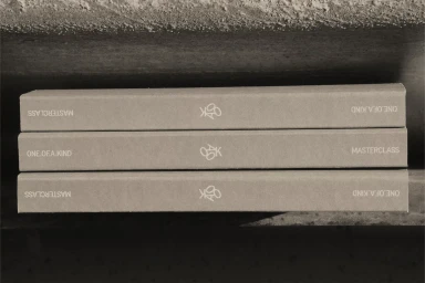 Three stacked light brown books with embossed white typography on a textured concrete surface.