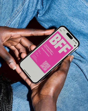 Close-up of a person holding a smartphone displaying a digital ticket with 'BFF' in pink, against a denim-clad background.