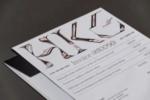Printed HKG Metals brand invoice with metallic chrome typography resting on a dark grey textured surface