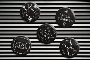 Five black circular badges featuring custom metallic typography and branding elements arranged on a corrugated metal background.