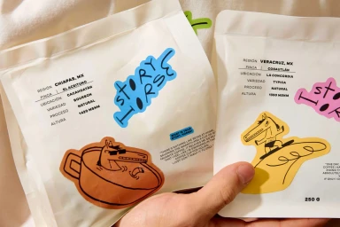 Two white coffee bags with colourful illustrated stickers held in hands for Story Horse brand identity project