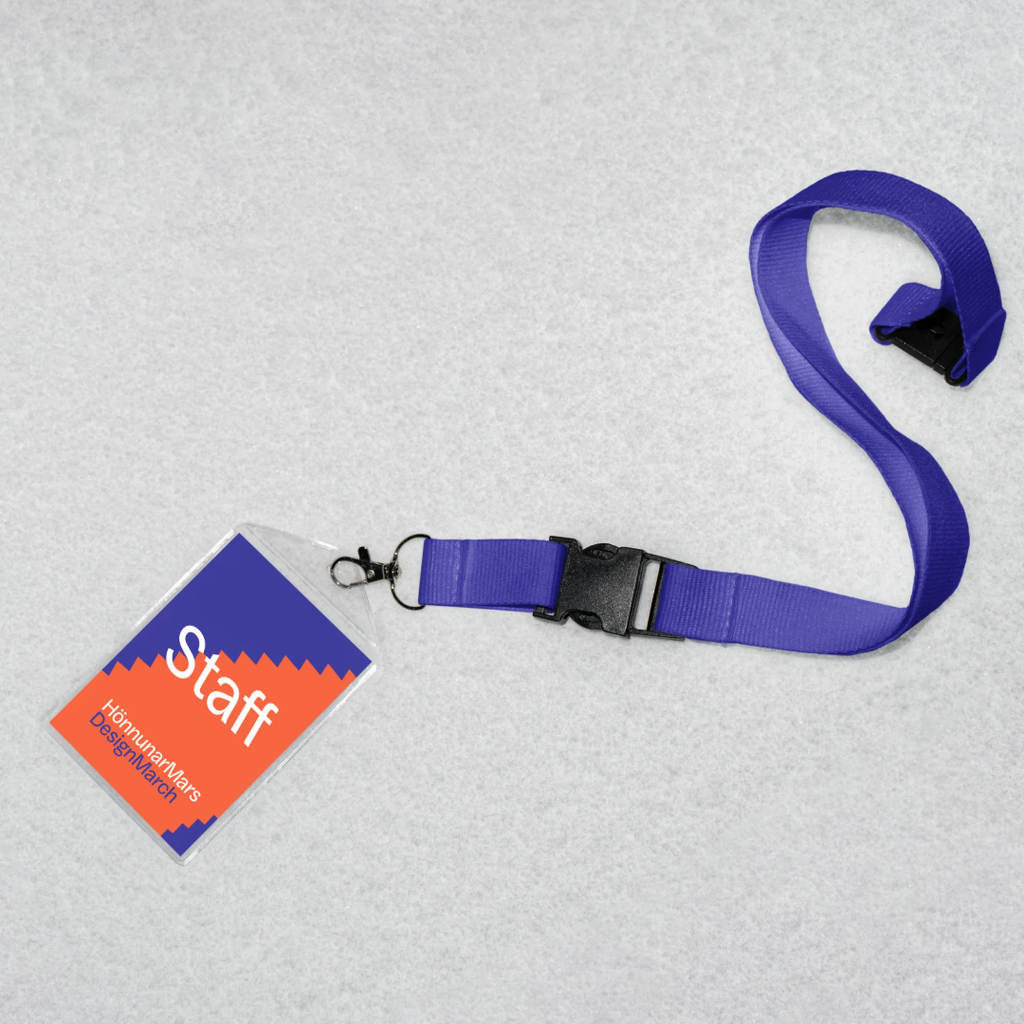 Staff ID badge with purple lanyard and a black buckle on a grey surface, showing the company name and role.