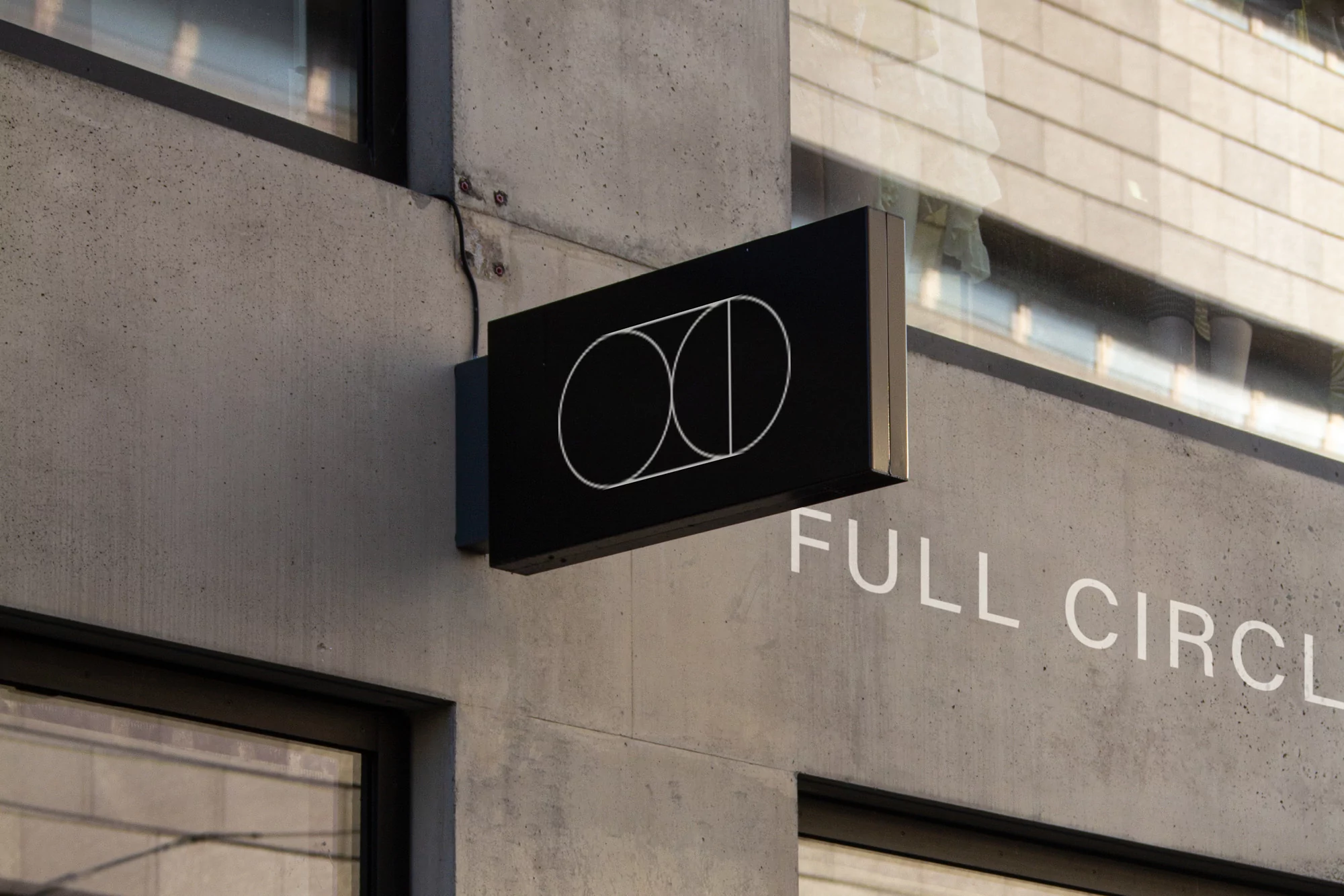 Close-up of a black sign with a white geometric logo consisting of two overlapping circles, mounted on a concrete exterior wall.