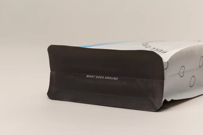 Close-up studio shot of a sealed package with black base and white upper section with graphic heart designs and the text 'What Goes Around'.