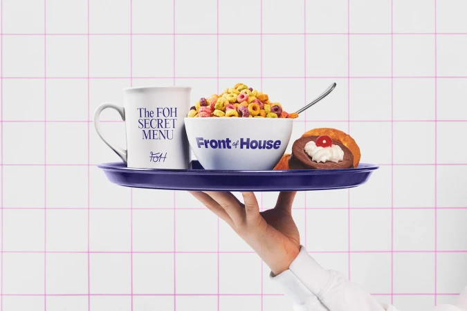 A hand holding a tray with a mug, bowl of cereal, donut, and pastry against a pink-lined white tiled background. Indoor food still life.