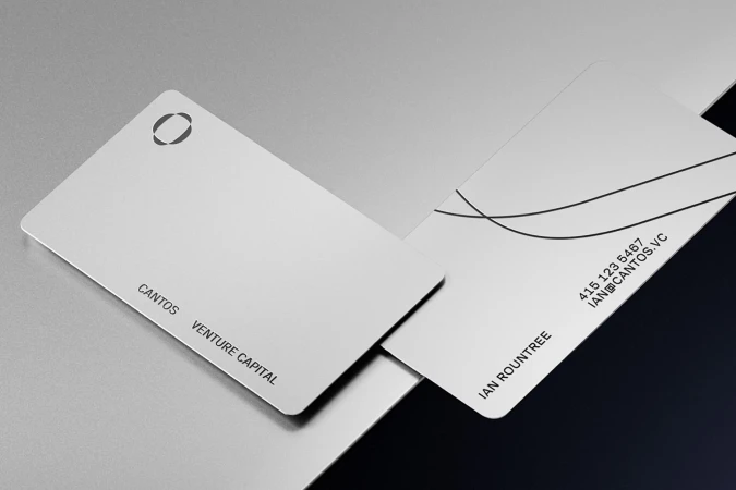 Two minimalist white business cards for Cantos resting on a sleek metallic surface
