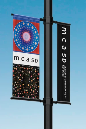 Street pole with two vertical banners for MCASD Museum of Contemporary Art San Diego against a clear blue sky on a sunny day.