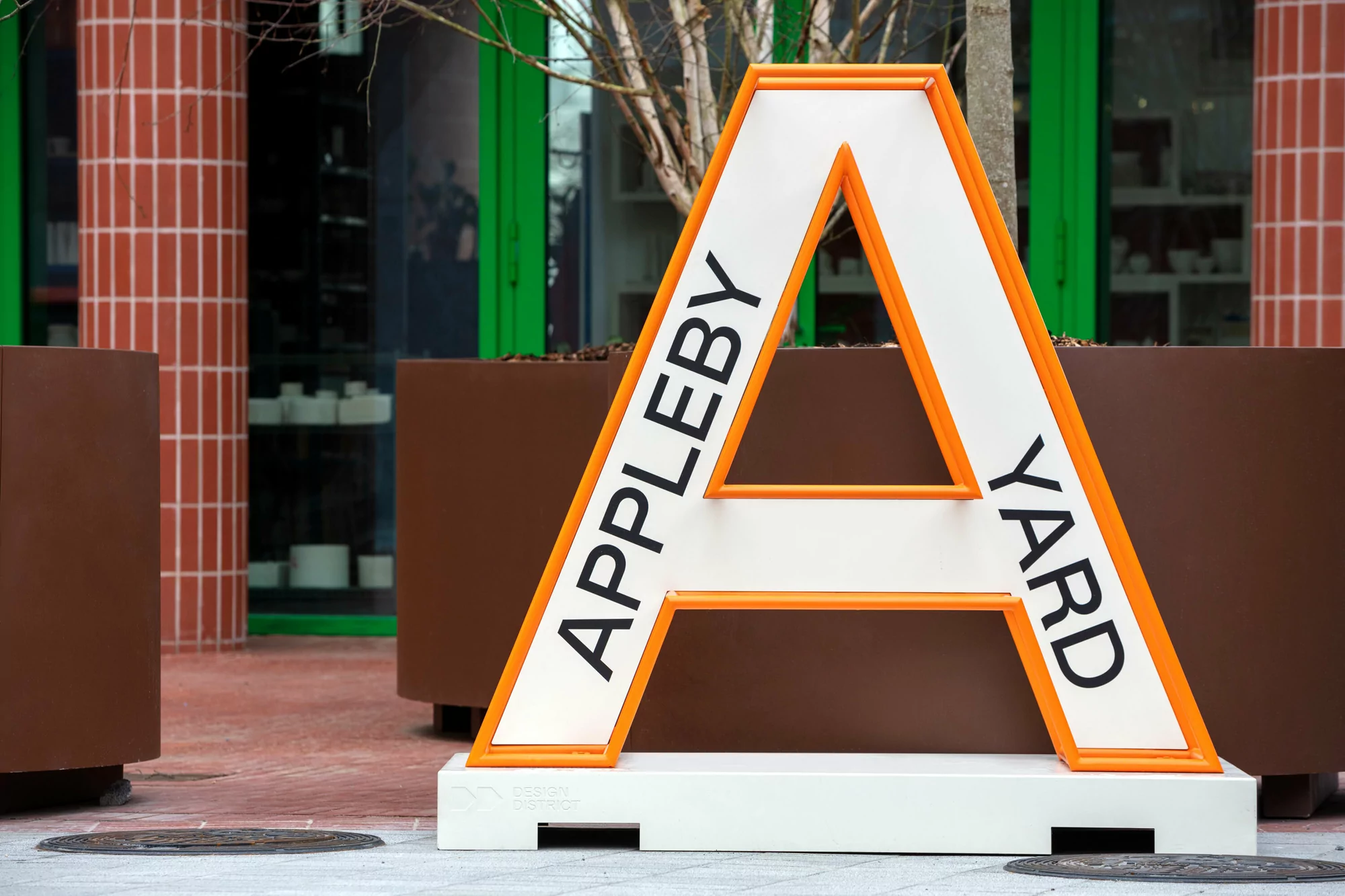 Large decorative sign reading APPLEBY YARD, standing outdoors in an urban environment with modern architecture in the background.