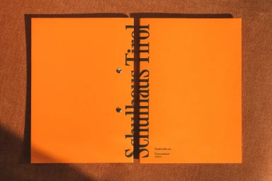 Bright orange folder with black typography resting on a textured brown fabric surface.