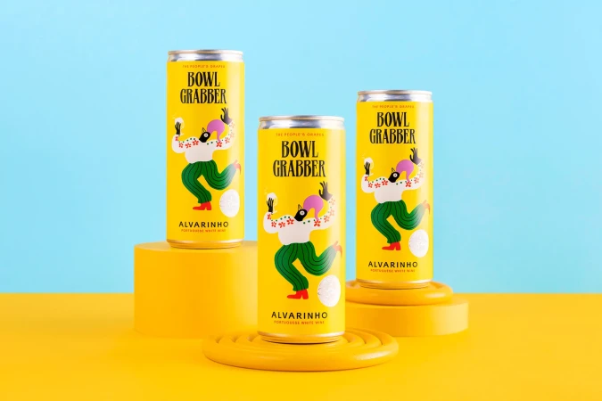 Three yellow cans of Alvarinho Portuguese white wine stand on yellow platforms against a split yellow and blue background, showcasing its packaging design.