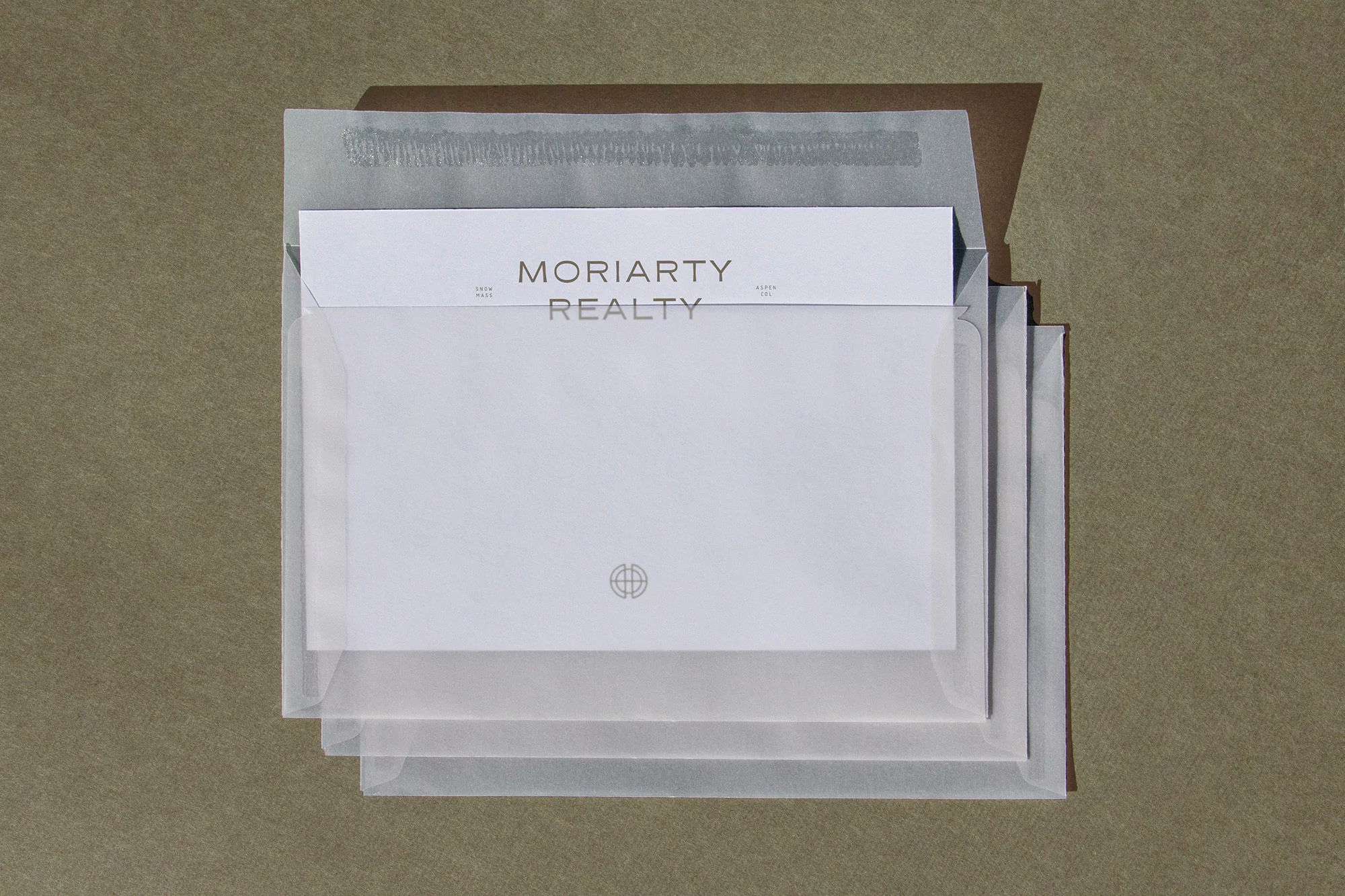 Letterhead stationery with 'Moriarty Realty' logo, transparent envelopes, and a textured tan background creates a clean, professional image.