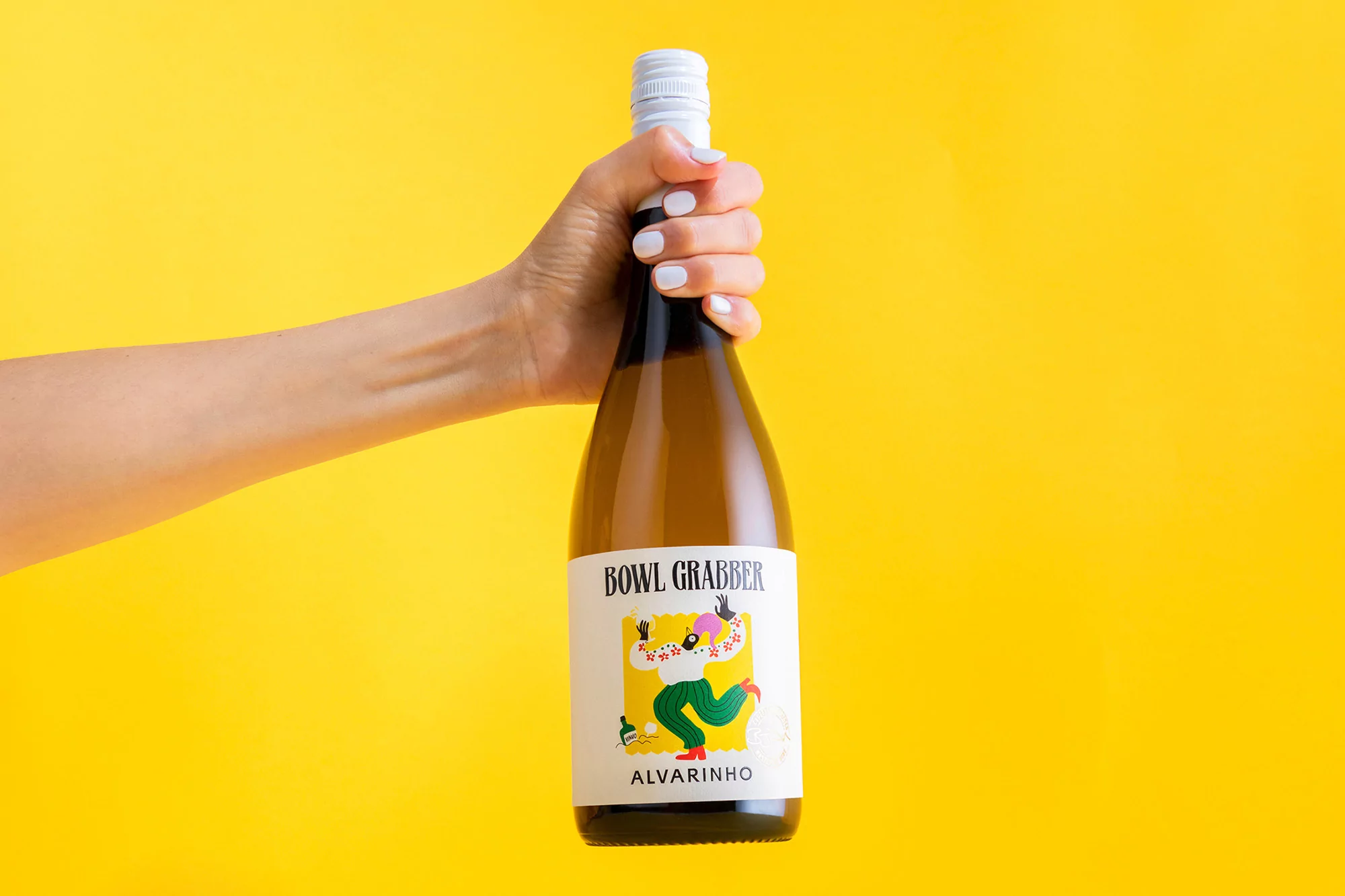 Close-up shot of a fair-skinned arm holding a white wine bottle with a colorful label against a vibrant yellow background.