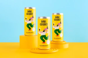 Three yellow canned wine cans with illustrated branding arranged on yellow risers against a blue and yellow backdrop.
