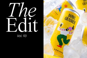 Yellow beverage cans labeled Bowl Grabber nestled amongst ice cubes next to a black panel with white serif text reading The Edit.