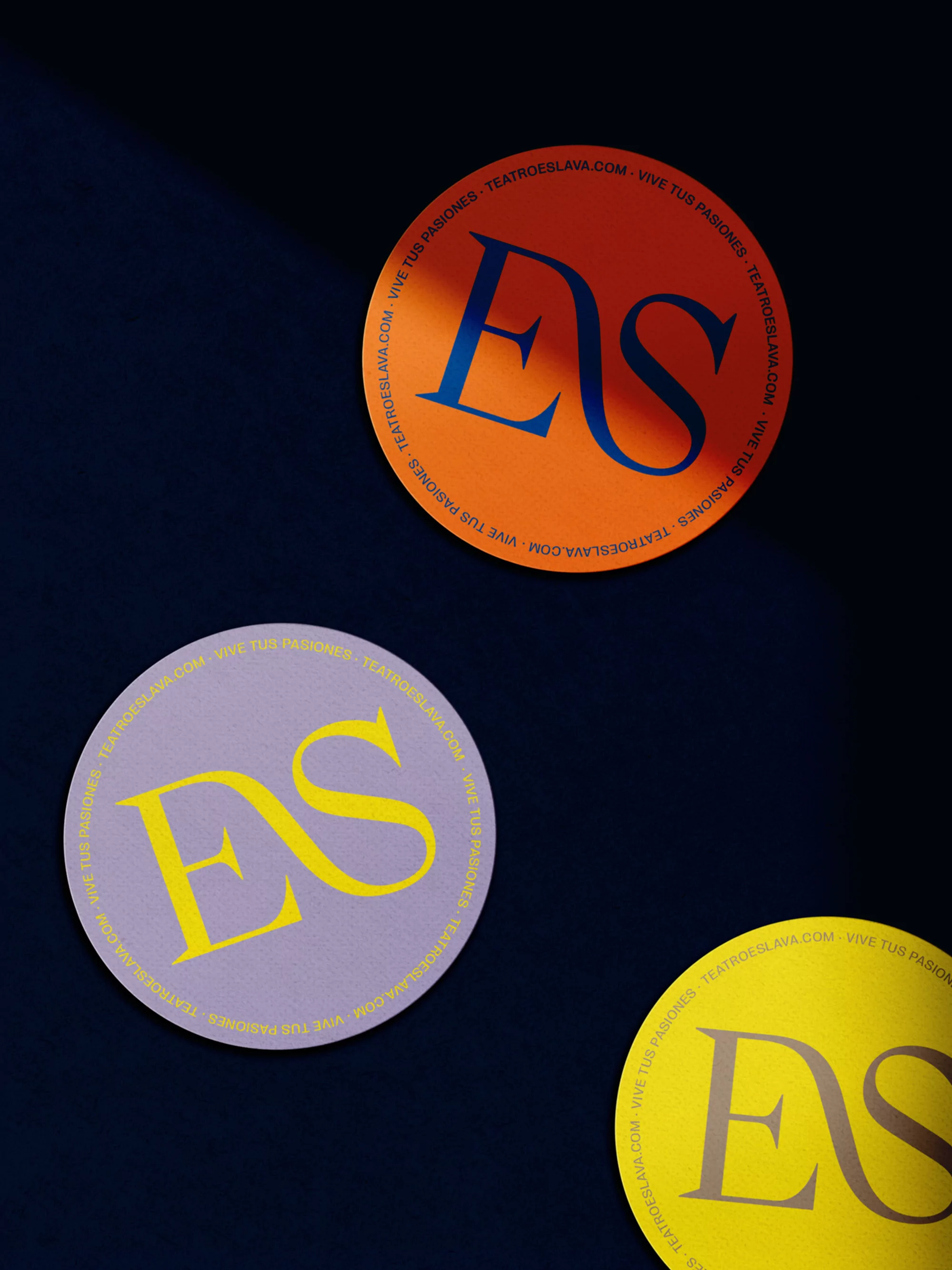 Three round logo stickers arranged on a dark blue surface featuring the letters ES in different colors on each sticker.