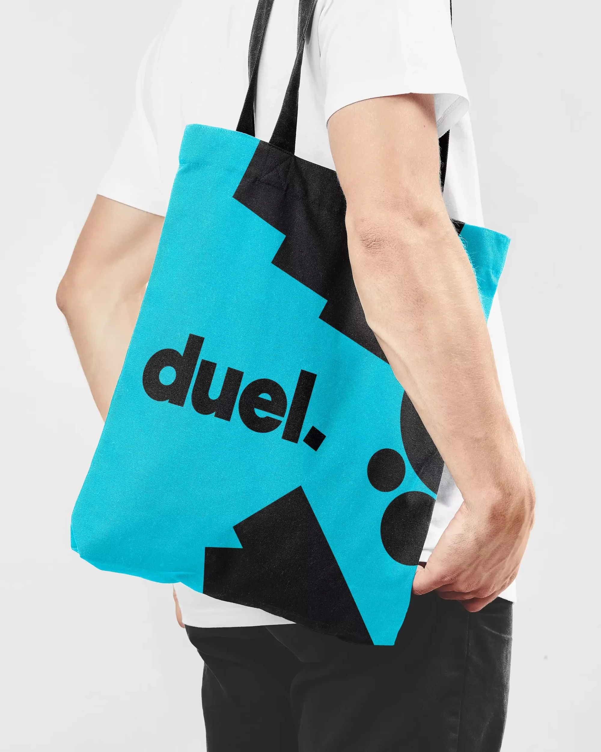 A person carries a bright turquoise tote bag with black graphics featuring the word 'duel' in bold font, paired with other design elements.