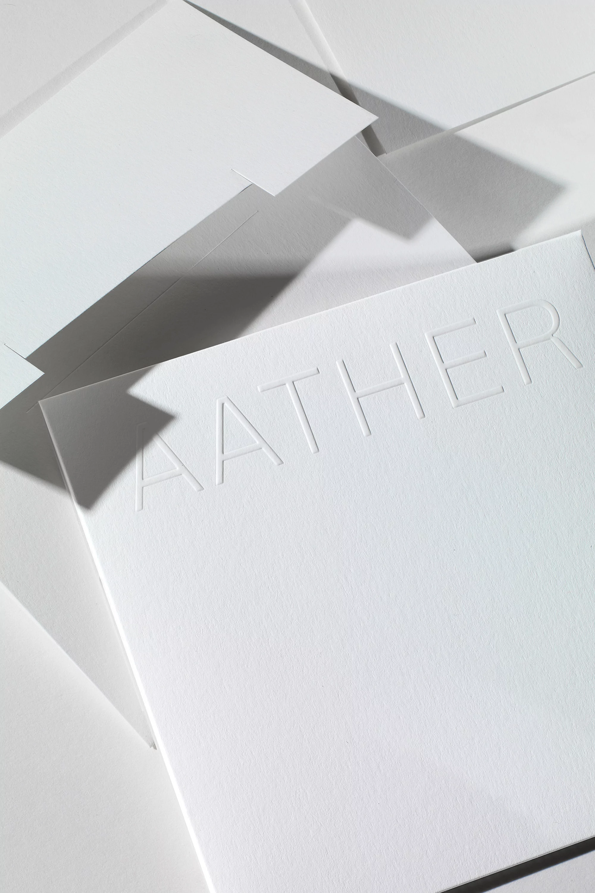 Close-up of several stacked, plain white cards under soft, directional lighting, one with the text 'AATHER' embossed on its surface.