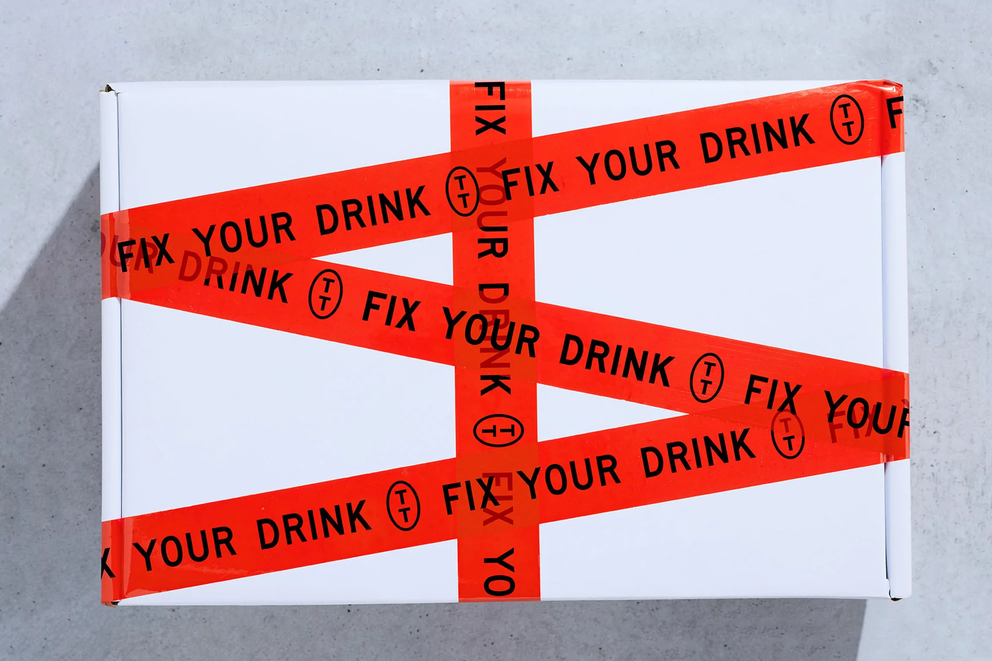 White box on a grey surface secured with red tape that reads 'Fix Your Drink'. The tape crisscrosses, creating a pattern across the box.