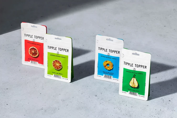 Four packets of Tipple Topper beverage garnishes in a row, featuring dried fruit slices in red, green, blue, and green packaging.