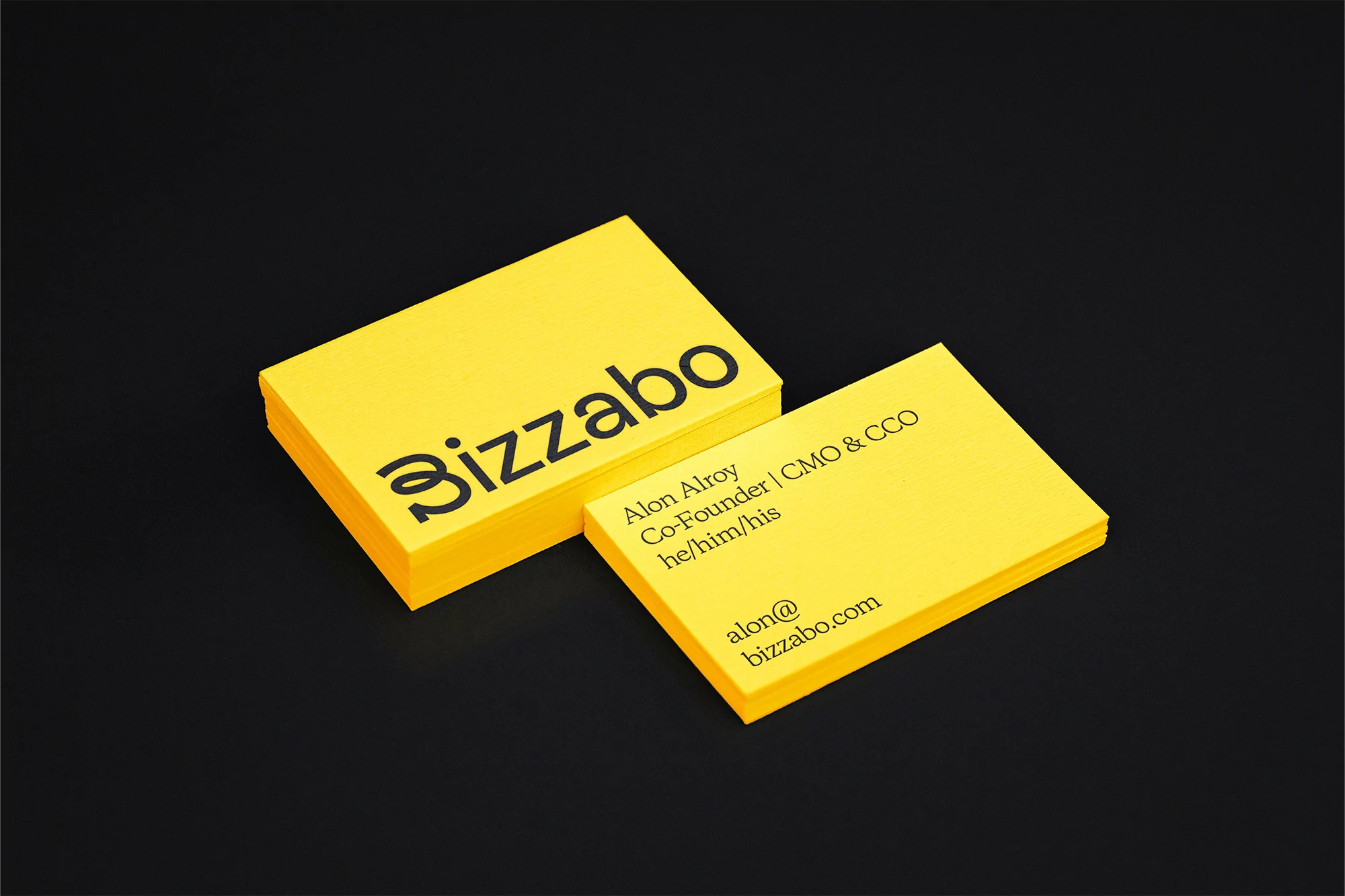 Stack of bright yellow business cards with black text and logo on a dark black background create a modern, minimalist design.