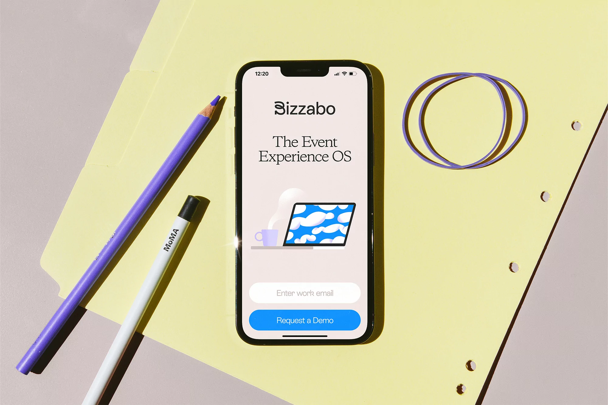 Smartphone displaying Bizzabo's event experience OS, paired with colorful office supplies on a yellow folder background.