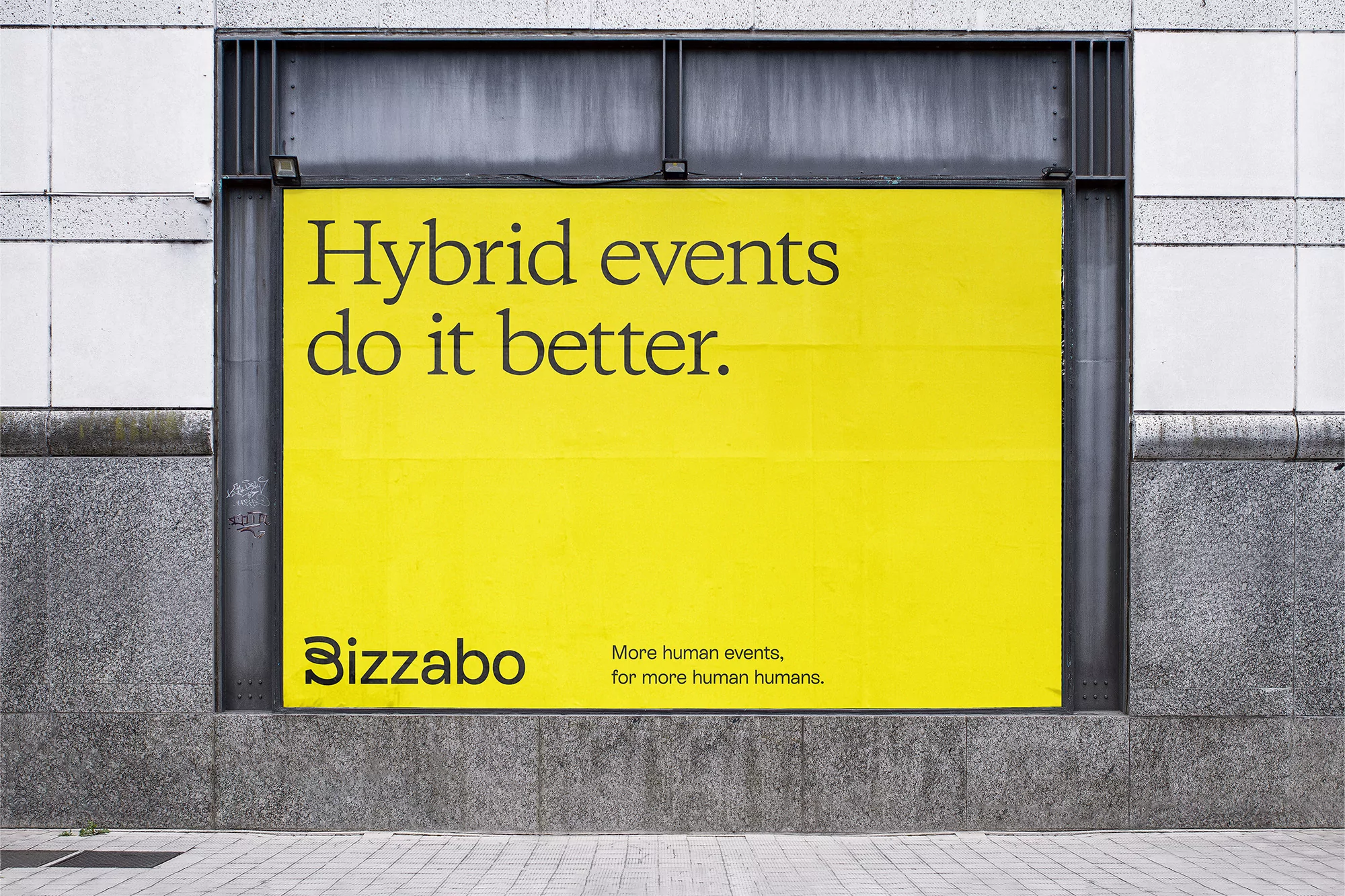 Bright yellow billboard on a grey stone wall with the words 'Hybrid events do it better' and 'Bizzabo' in black letters.