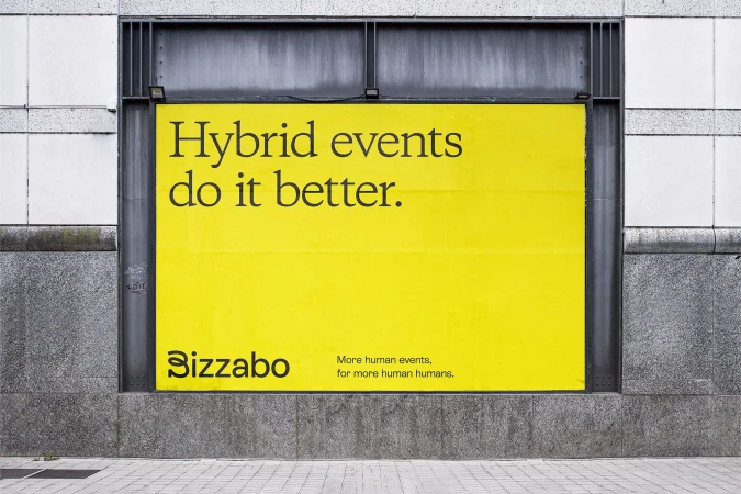 Bright yellow billboard on a grey stone wall with the words 'Hybrid events do it better' and 'Bizzabo' in black letters.
